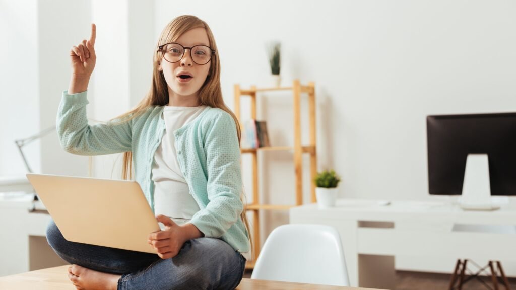 A young child eagerly raising a hand while learning math on a laptop