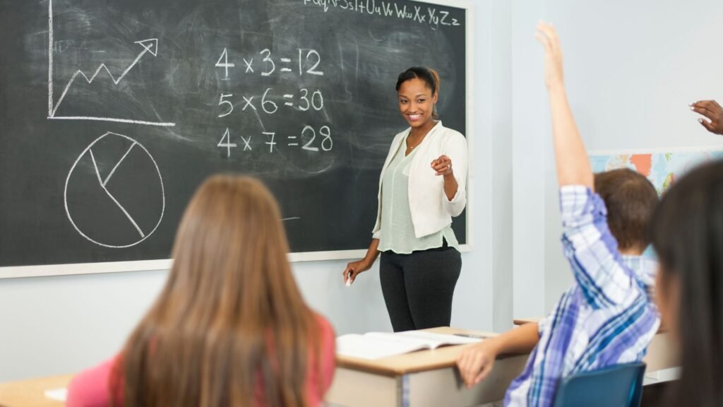 A teacher explaining math word problems on a chalkboard to a class
